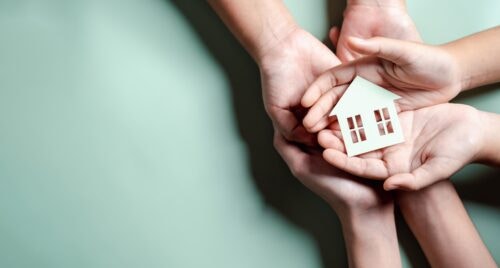 Hands holding wooden house, family home, homeless housing, mortgage crisis and home protecting insurance, international day of families, foster home care, family day care, stay home concept