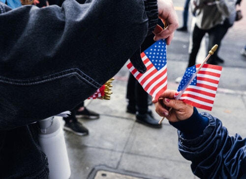 One person hands miniature American flags to another, with only their arms visible.